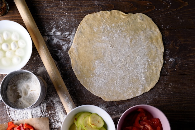 Estendeu um grande círculo de massa com espaço para texto em uma mesa de madeira com ingredientes para pizza ou torta. vista superior, Flatley.