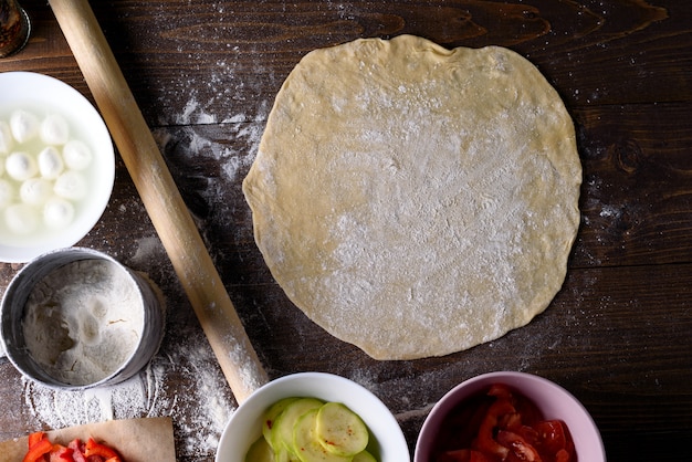 Estendeu um grande círculo de massa com espaço para texto em uma mesa de madeira com ingredientes para pizza ou torta. vista superior, flatley.