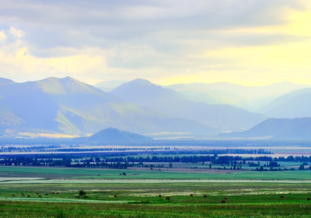 Estepa herbosa entre montañas azules en niebla, cielo nublado al atardecer. Siberia, Rusia