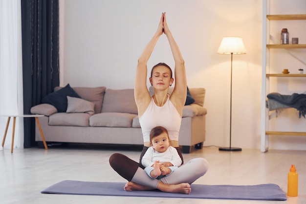 En la estera de yoga Madre con su pequeña hija está en casa juntos