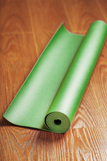 Una estera de yoga verde se coloca en un rollo sobre el piso de madera. Un estilo de vida saludable de forma aislada.