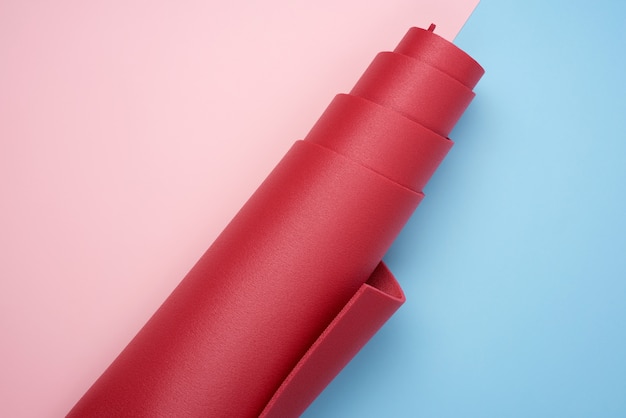 Esterilla de neopreno rojo retorcido para yoga y deportes sobre fondo azul rosa
