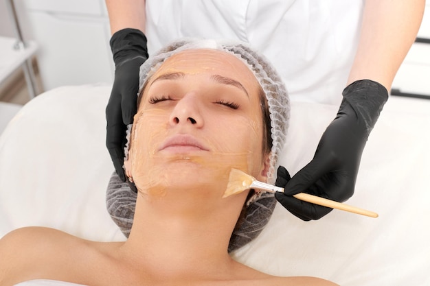 Esteticista aplica máscara de miel en la cara de la mujer para hidratar la piel de la cara en el salón de belleza spa