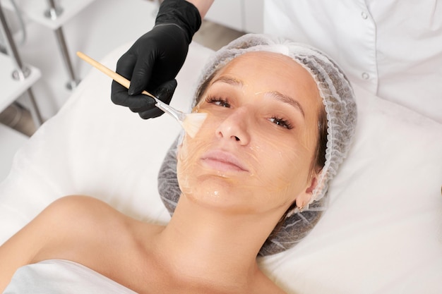 Esteticista aplica máscara de miel en la cara de la mujer para hidratar la piel de la cara en el salón de belleza spa