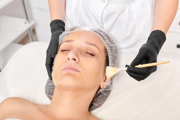 Esteticista aplica máscara de miel en la cara de la mujer para hidratar la piel de la cara en el salón de belleza spa