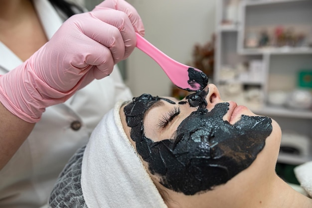 Esteticista aplica una máscara negra a la cara de su cliente en un salón de belleza