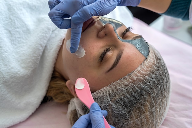 Esteticista aplicando crema curativa en un cliente de rostro femenino joven.