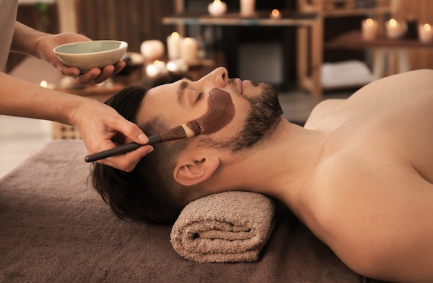 Esteticista aplicando mascarilla cosmética en el rostro del hombre en el salón de spa