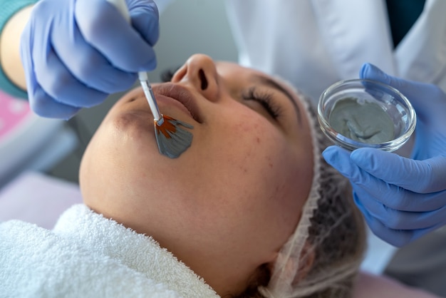 Esteticista aplicando mascarilla facial para clienta en el salón de spa. Cuidado de la salud