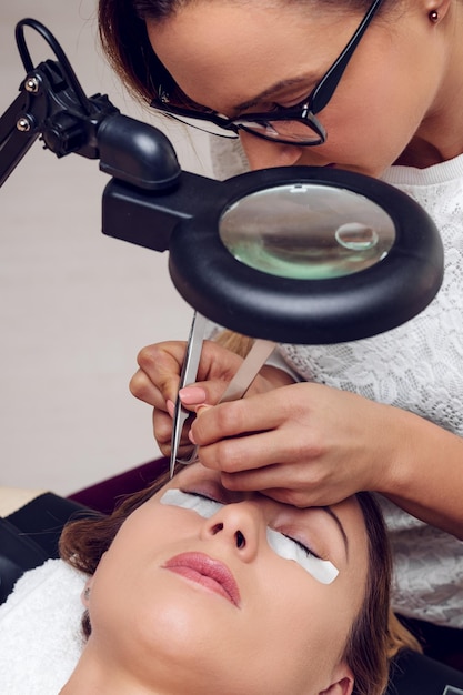 Esteticista aplicando pestañas extendidas al modelo en el salón de belleza.