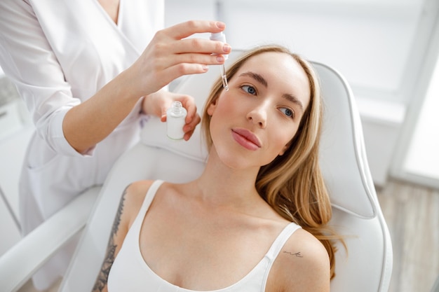 Esteticista aplicando suero vitamínico en la cara de la mujer