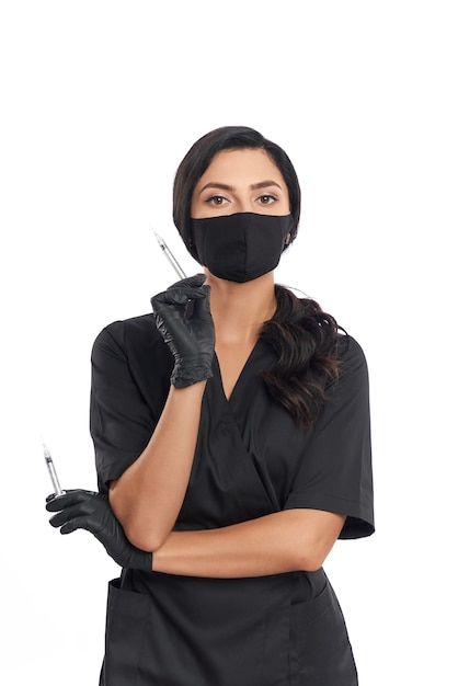 Esteticista competente en uniforme médico, máscara y guantes sosteniendo jeringas con dos manos para el cuidado de la piel