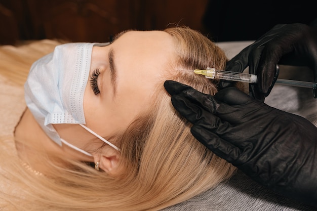 Esteticista de luvas dá injeção na cabeça de uma mulher loira. Mesoterapia, terapia da queda de cabelo. Conceito de restauração capilar.