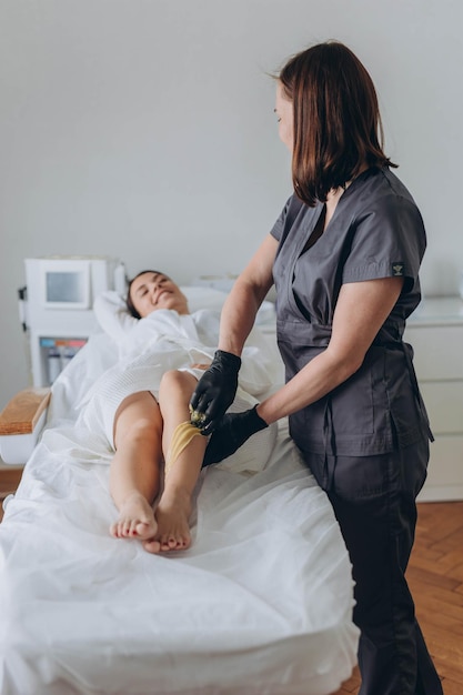 Esteticista depilando las piernas de la mujer joven con azúcar líquido en el centro de spa