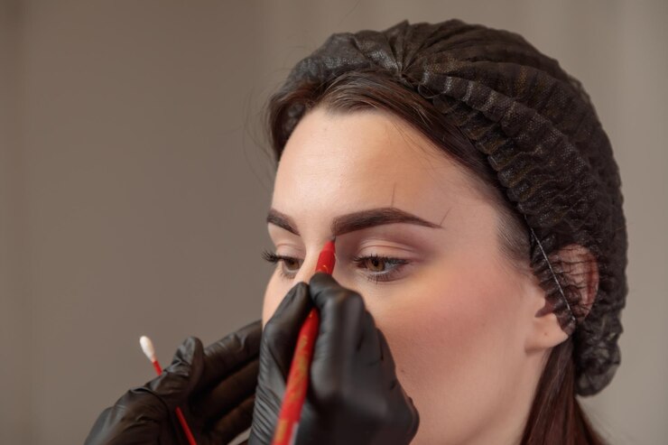 Foto esteticista desenhando a forma da sobrancelha no rosto da mulher para tratamento de microblading