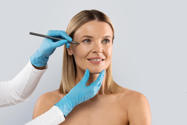 Esteticista dibujando líneas bajo los ojos de una mujer de mediana edad