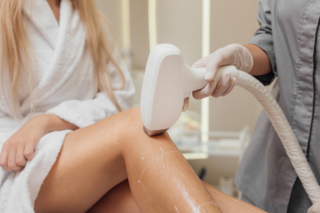 Esteticista elimina el vello en hermosas piernas femeninas usando una depilación láser en una clínica de belleza