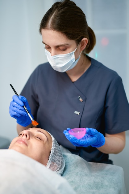 Esteticista está aplicando una crema saludable en la piel del rostro femenino