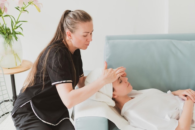 Esteticista faz creme facial, de massagem e cosmético para uma adorável jovem com uma toalha na cabeça