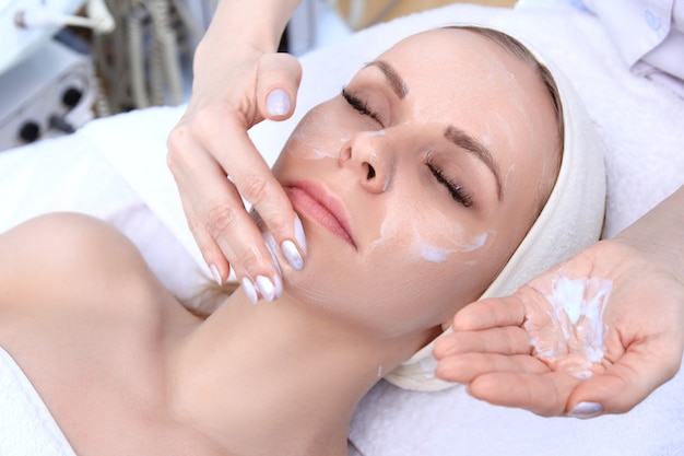 Esteticista faz limpeza e esfoliante facial para linda garota. Salão de beleza.