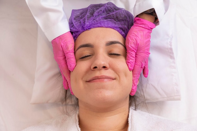 Esteticista faz uma massagem profissional do rosto do pescoço e ombros para uma jovem no salão Spa A vista do topo Tratamento de beleza facial