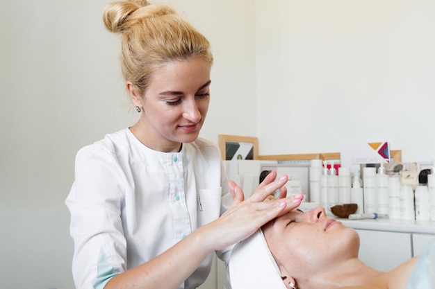 Esteticista feminina fazendo massagem facial sua cliente feminina em uma clínica de beleza