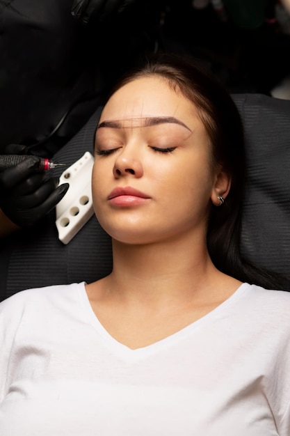 Esteticista en guantes aplicando maquillaje de cejas en polvo permanente