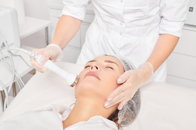 Esteticista hace estiramiento de la piel por ultrasonido para rejuvenecer la cara de la mujer usando fonoforesis