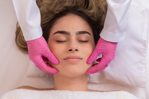 Esteticista hace un masaje profesional de la cara del cuello y los hombros para una joven en el salón Spa La vista desde arriba Tratamiento de belleza facial