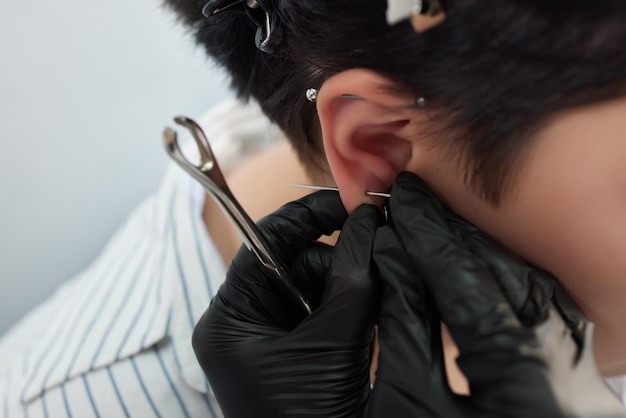 Una esteticista hace una punción en el lóbulo de la oreja con un dispositivo desechable en un salón de belleza.