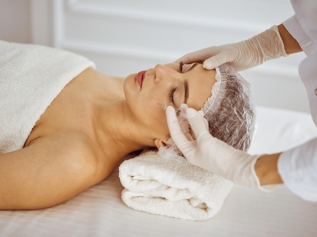 Esteticista haciendo procedimiento de belleza con jeringa en la cara de una joven morena. Medicina y cirugía estética, inyecciones de belleza.