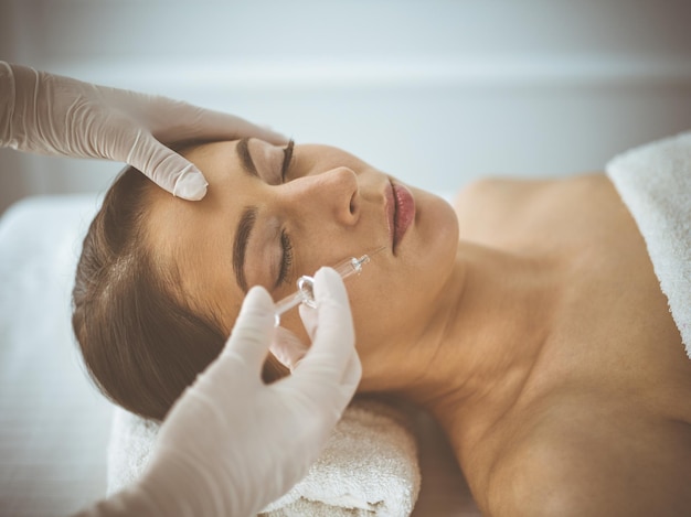 Esteticista haciendo procedimiento de belleza con jeringa en la cara de una joven morena. Medicina y cirugía estética, inyecciones de belleza.