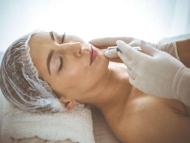 Esteticista haciendo procedimiento de belleza con jeringa en la cara de una joven morena. Medicina y cirugía estética, inyecciones de belleza.