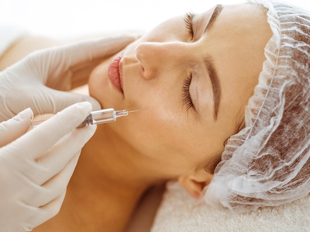 Esteticista haciendo un procedimiento de belleza con una jeringa en el rostro de una joven morena. Medicina cosmética y cirugía, inyecciones de belleza.