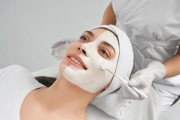 Esteticista haciendo procedimiento de cara de máscara para mujer joven