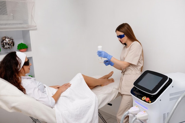 Esteticista haciendo procedimiento de depilación en piernas para mujer cliente Depilación láser y cosmetología en salón de belleza