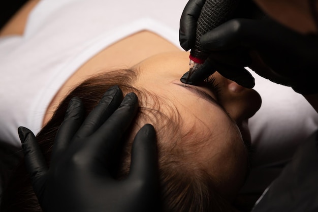 Foto esteticista haciendo tatuaje de cejas permanente a una mujer