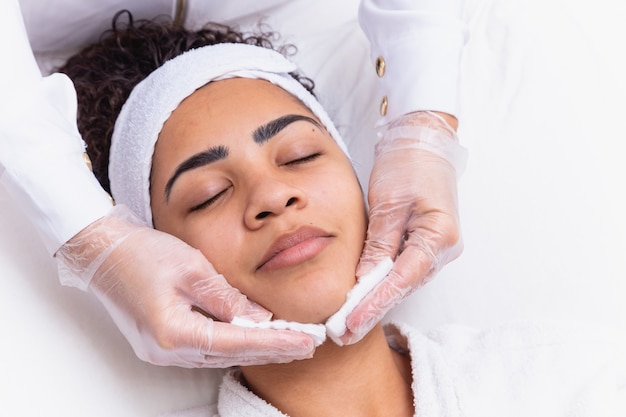 Esteticista, limpando o rosto da mulher com algodão. Mulher no spa, fazendo limpeza facial.