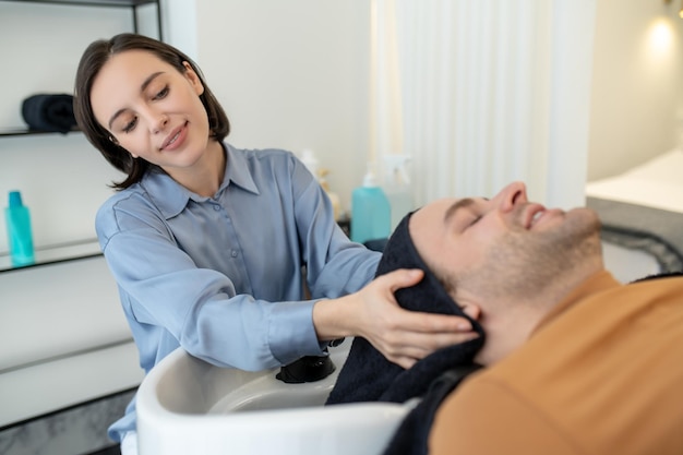 Esteticista masajeando la cabeza del hombre durante los procedimientos de tratamiento del cabello