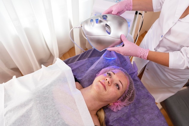 Foto una esteticista pone una máscara facial de led en una mujer para el cuidado de la piel tratamiento de terapia de luz