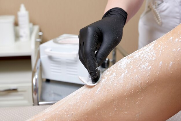 Esteticista preparándose para depilar las piernas femeninas en el centro de spa. preparación para la depilación, poniendo un poco de polvo blanco.