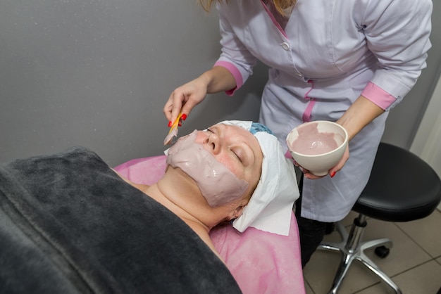 Una esteticista profesional aplica una mascarilla de alginato en la cara del cliente.
