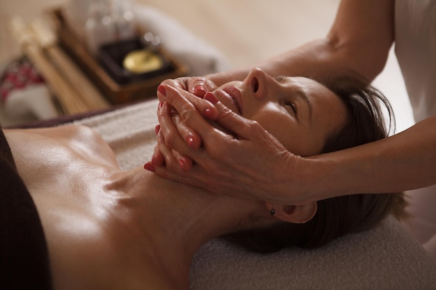 Esteticista profesional irreconocible haciendo masajes faciales para mujeres maduras, trabajando en el centro de spa