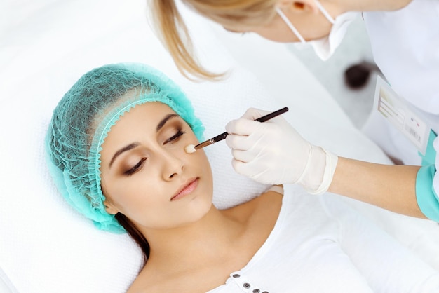 Esteticista profissional está fazendo procedimento cosmético em formação médica leve tocando o rosto do paciente com pincel, closeup. Tratamento de cosmetologia.