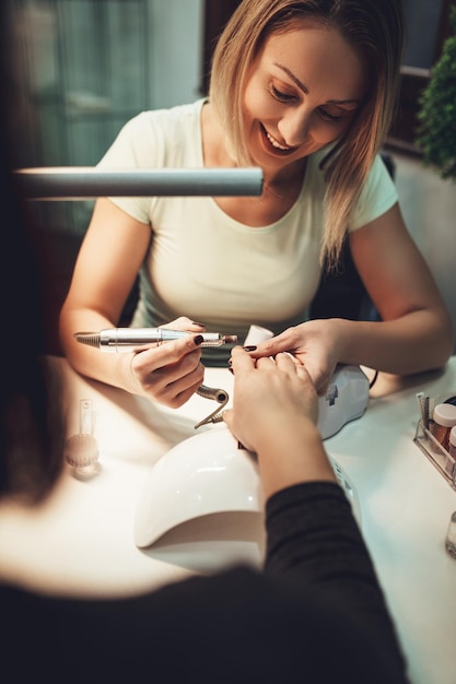 Foto esteticista puliendo las uñas de las clientas con una lima de uñas en el salón de belleza.