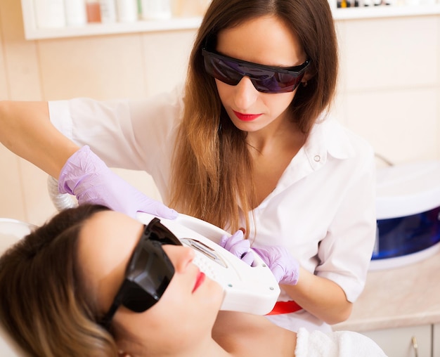 Foto esteticista quitando el pelo del tratamiento de depilación láser de la mujer joven en la clínica de belleza cosmética