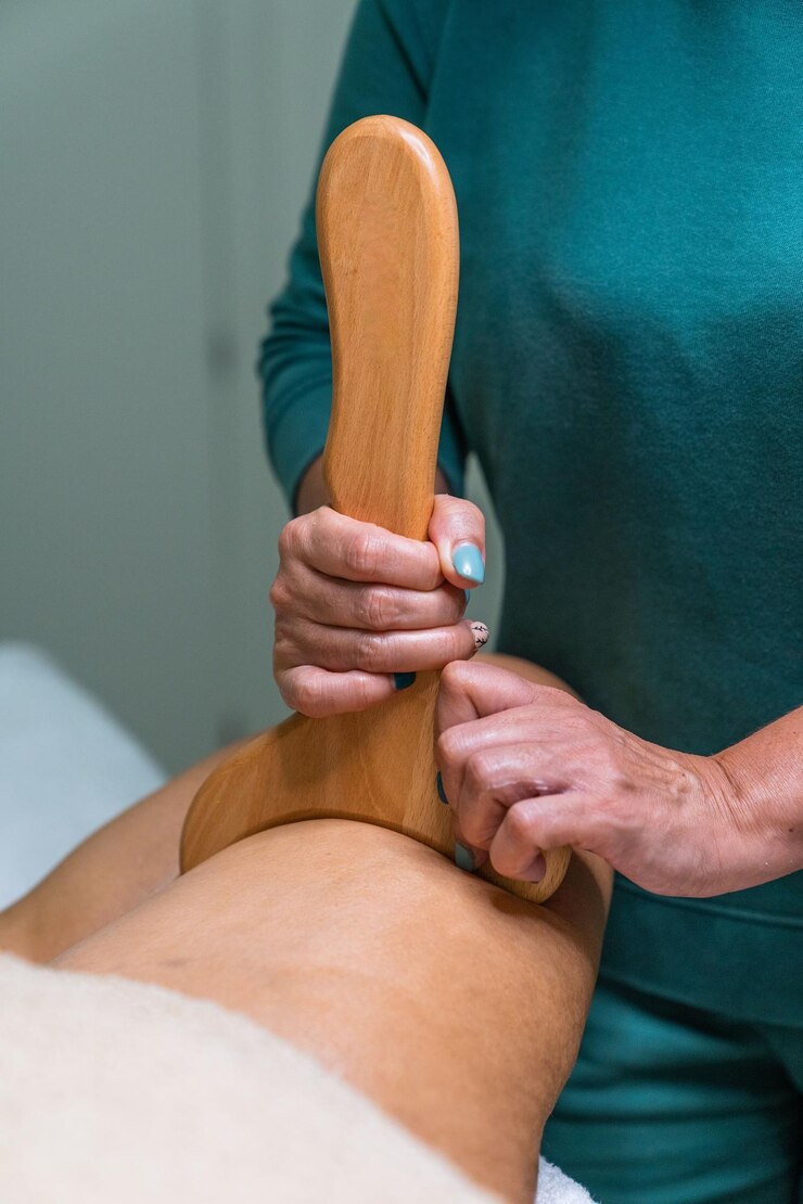 Foto esteticista realizando tratamento de terapia de madeira com a tábua de moldagem na perna do paciente