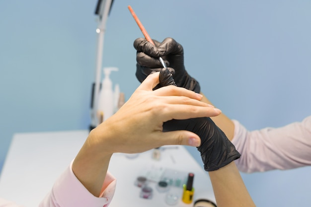 Esteticista en salón de belleza haciendo manicura, pinta uñas