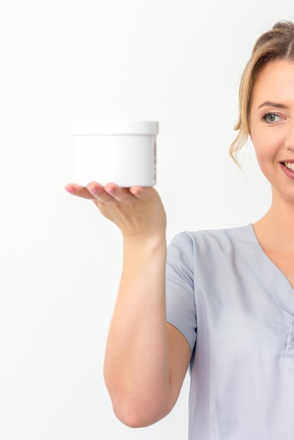 Esteticista segurando um frasco de cera para depilação sorrindo sobre um produto natural de fundo branco