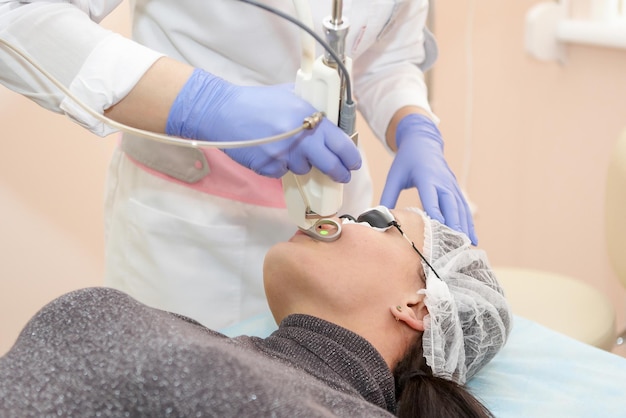 Esteticista terapeuta hace un rejuvenecimiento láser para la Mujer por aparato en un salón de belleza